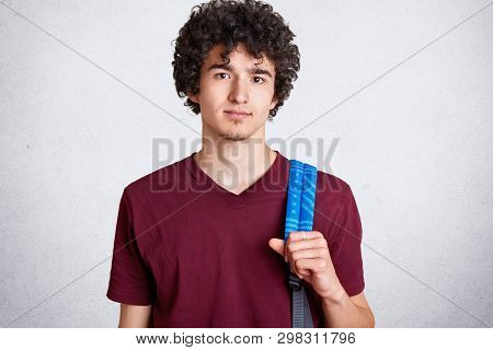 Portrait Of Attractive Caucasian Man With Blue Backpack, Has Dark Curly Hair, Looking Directly At Ca