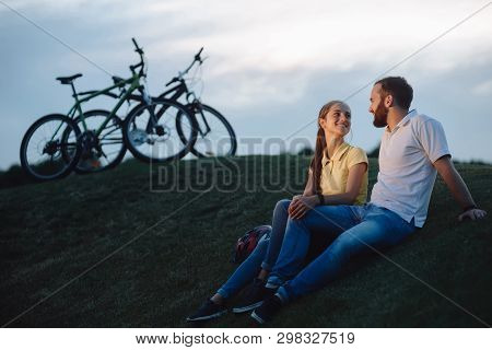 Couple Of Cyclists In Love Resting On Green Hill. The Pair Finished The Bike Ride On The Green Meado