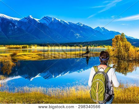 Shores of Abraham Lake in the Rocky Mountains. Canada. Middle-aged woman with a large green tourist backpack admires the lake. Concept of active, ecological and photo tourism