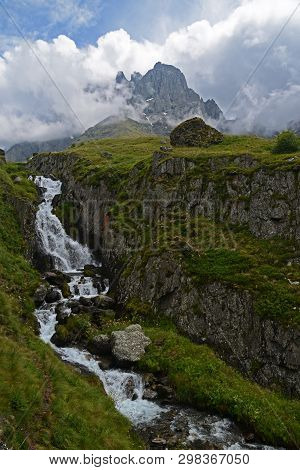 Waterfall Among Green Rocks. Massive Shrouded Rock In The Background.