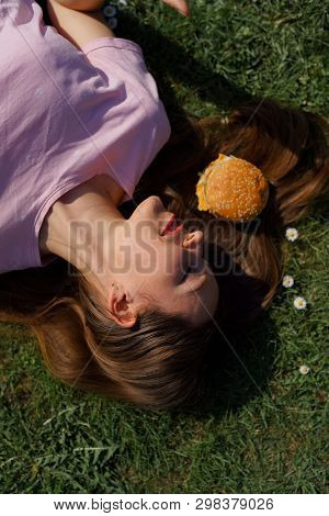 Successful Business Woman Lying On Grass With Fast Food Burger Cheesburger On Hair Enjoying Leisure 