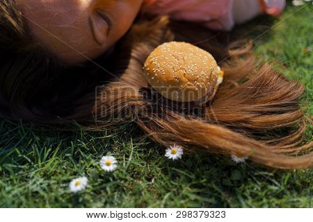 Successful Business Woman Lying On Grass With Fast Food Burger Cheesburger On Hair Enjoying Leisure 