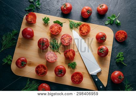 Tasty Ripe Tomatoes Sliced On Chopping Board With Greenery, Sharp Knife Near, Isolated Over Dark Bac