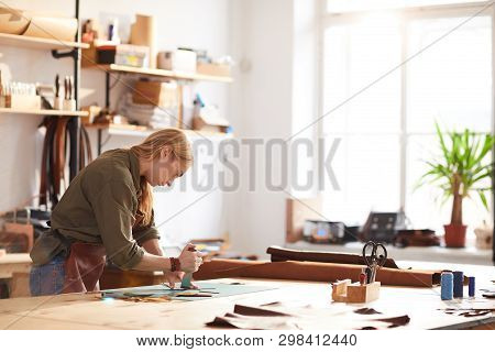 Side View Portrait Of Young Woman Cutting Leather Patterns In Atelier Workshop Lit By Sunlight, Copy