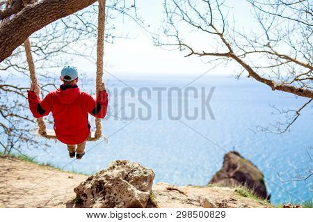 The Guy In The Red Jacket Rides On The Chela Overlooking The Sea And Rocks.