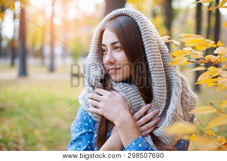 Cute Beautiful Smile Woman Walking In Yellow Autumn Park. Girl In Knitten Scarf Near Tree And She Is