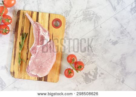 Piece Raw Meat On Cutting Board With Rosemary. Uncooked Fresh Pork Bone Steak With Tomato On Stone B