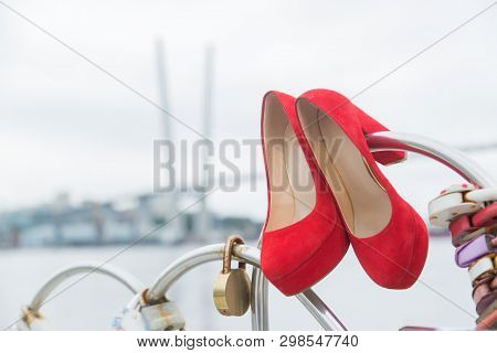 Red Luxury Shoes Hanging On The Fence With Locks Of Hearts Against The Sky