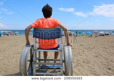 Young Boy On The Wheelchair On The Beach With Orange T-shirt