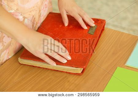 The Woman Put Her Hands On The Red Cover Of A Photo Book Or Album, On The Desk. The View From The To