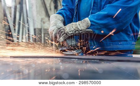 Worker in metal factory grinding workpiece with disk grinder, sparks flying