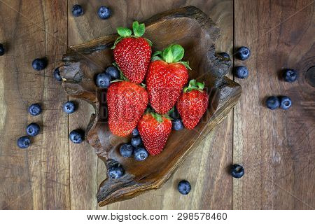 A Small Wooden Bowl Of Blueberries Is Surrounded By Fresh Healthy Strawberries On A Rustic Wood Plan