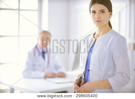 A Doctor Looking At The Camera With Her Male Colleage In The Back Of The Conference Room In Hospital