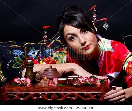 Beautiful young woman in red Asian costume arranging Japanese tea ceremony
