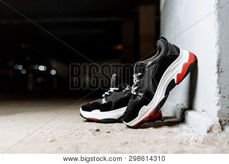 Black Sneakers On A Thick White Sole With Red Inserts On A Concrete Background Are Supported On A Wh