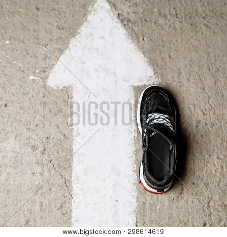 Black Sneaker On A Thick White Sole With Red Accents On A Concrete Background Near A Painted White A