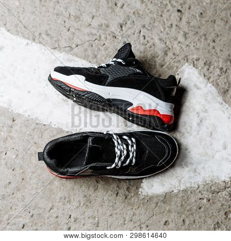 Black Sneakers On A Thick White Sole With Red Accents On A Concrete Background Near A Painted White 