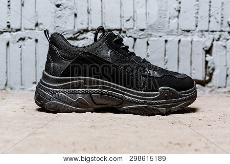 Black Sneaker With Thick Soles On The Cement Floor Against The Background Of Brick Wall