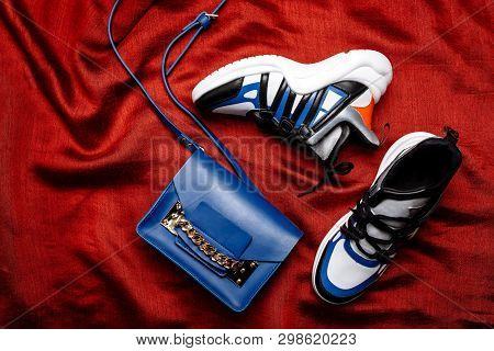 White Sneakers With Black And Blue Inserts On A Thick Figured Sole And A Blue Bag With A Gold Chain