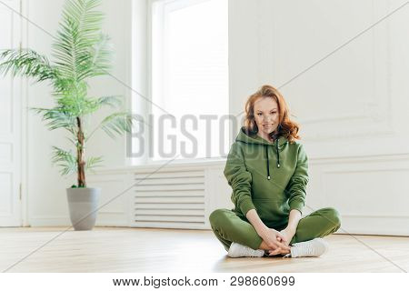 Beautiful Satisfied Slim Woman With Ginger Hair, Appealing Appearance, Sits Crossed Legs, Wears Gree