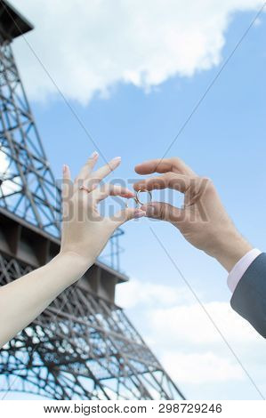 A Man And A Woman With Wedding Rings Next To Each Other. Background With The Eiffel Tower. Ornaments