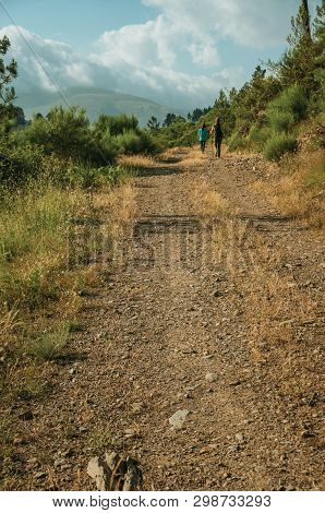 People Hiking On Dirt Road Through Hilly Landscape