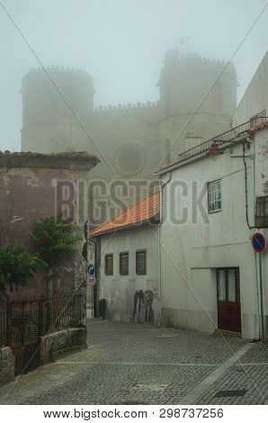 Guarda, Portugal - July 20, 2018. Cathedral Behind Worn Old Houses On Alley, In The Morning Mist Of 