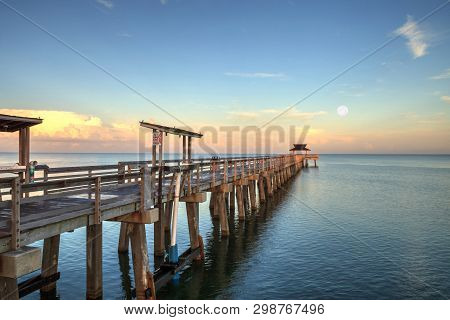 Early Moonset And Sunrise Over The Naples Pier On The Gulf Coast Of Naples, Florida In Summer.