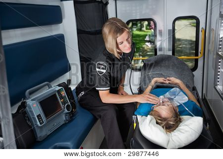 Female EMT worker tending to ill senior patient, listening to heart rate with stethoscope