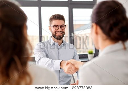 new job, hiring and employment concept - team of recruiters having interview with male employee and shaking hands at office