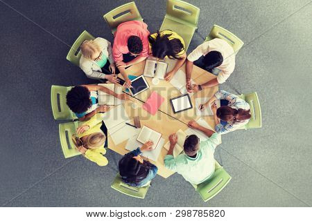 education, high school, people and technology concept - group of international students sitting at table with tablet pc computers, books and notebooks at university library from top