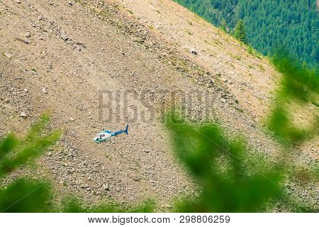 Helicopter In Air Against Background Of Rocky Mountain. Rescue Mission In Mountains. Mountainous Aer