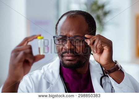 Doctor Wearing Glasses Looking At Ampoule Checking The Liquid