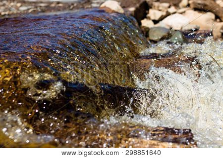 Clean River Water Flows Over The Stones And Envelops Them. Bright Sun Rays Are Reflected In The Flow