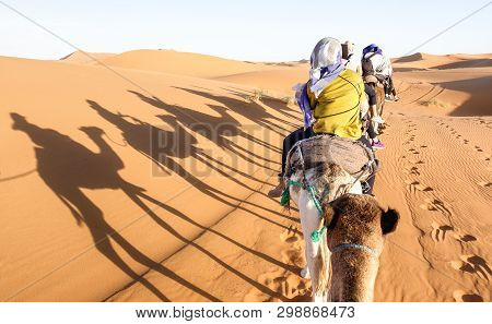 Tourists Caravan Riding Dromedaries Through Sand Dunes In Sahara Desert Near Merzuga In Morocco - Wa