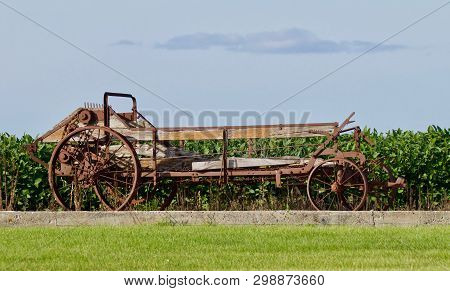 An Antique Manure Spreader Sits In Front Of A Soybean Field.