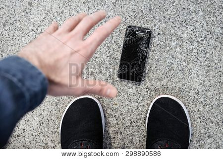 Young Man Picks Up His Broken Smartphone With Cracked Screen Glass After Falling.
