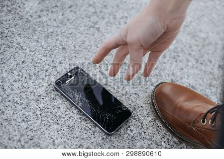Young Woman Picks Up Her Broken Smartphone With Cracked Screen Glass After Huge Falling.