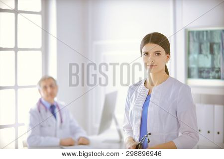 A doctor looking at the camera with her male colleage in the back of the conference room in hospital