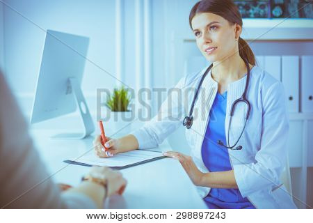 Doctor and patient discussing medical problems in a hospital consulting room. Doc filling in a patient's form
