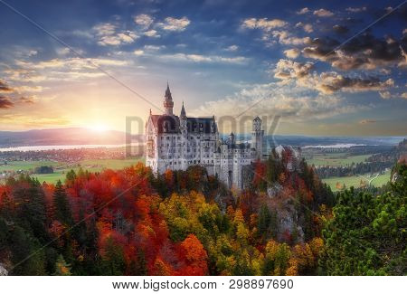 Tipical Postcard. Majestic Neuschwanstein Castle During Sunset, With Colorful Clouds Under Sunlight.