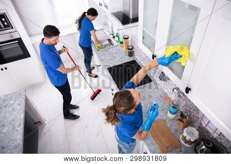 Group Of Young Janitors In Uniform Cleaning Kitchen At Home