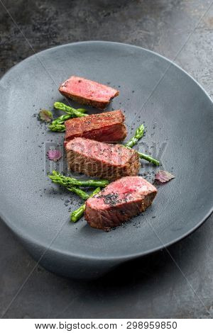 Barbecue dry aged wagyu fillet steak with blanched green asparagus tips and herbs as closeup on a modern design plate with copy space