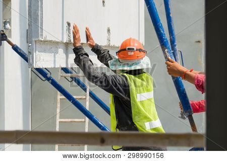 Construction Worker Are Installing The Precast Concrete Wall, Orange Safety Helmet And Green Vest.
