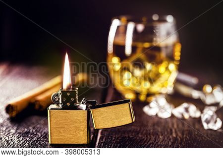 Vintage Windproof Access Lighter On Rustic Wooden Background. Cigar And Glass Of Alcohol In The Back