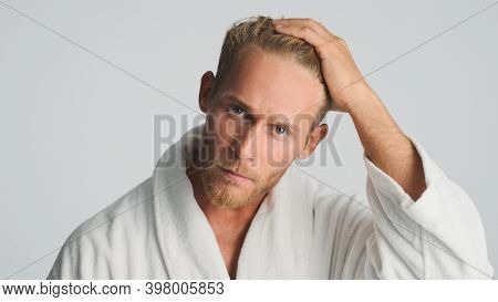 Attractive Bearded Man In Bathrobe Looking Serious Preening On Camera Over White Background