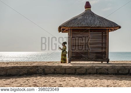 African Woman Standing Next To A Bungalow Alone Wearing African Clothes On The Coast Of Africa In Ke