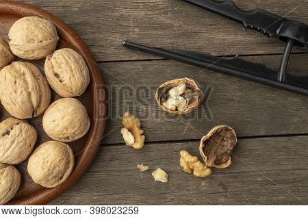 Walnuts, Nut Cracker And Cracked Nuts Over Wooden Table.