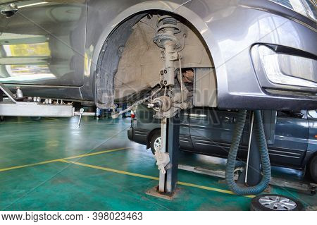 A Grey Car With The Front Right Steering Knuckle And Wheel Removed Hangs On A Lift In An Auto Repair