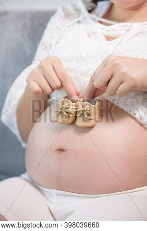 Pregnant Woman Holding Small Baby Shoes Relaxing At Home